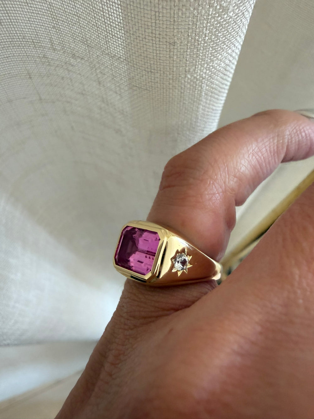 A ring worn on the hand against a sunlit curtain.