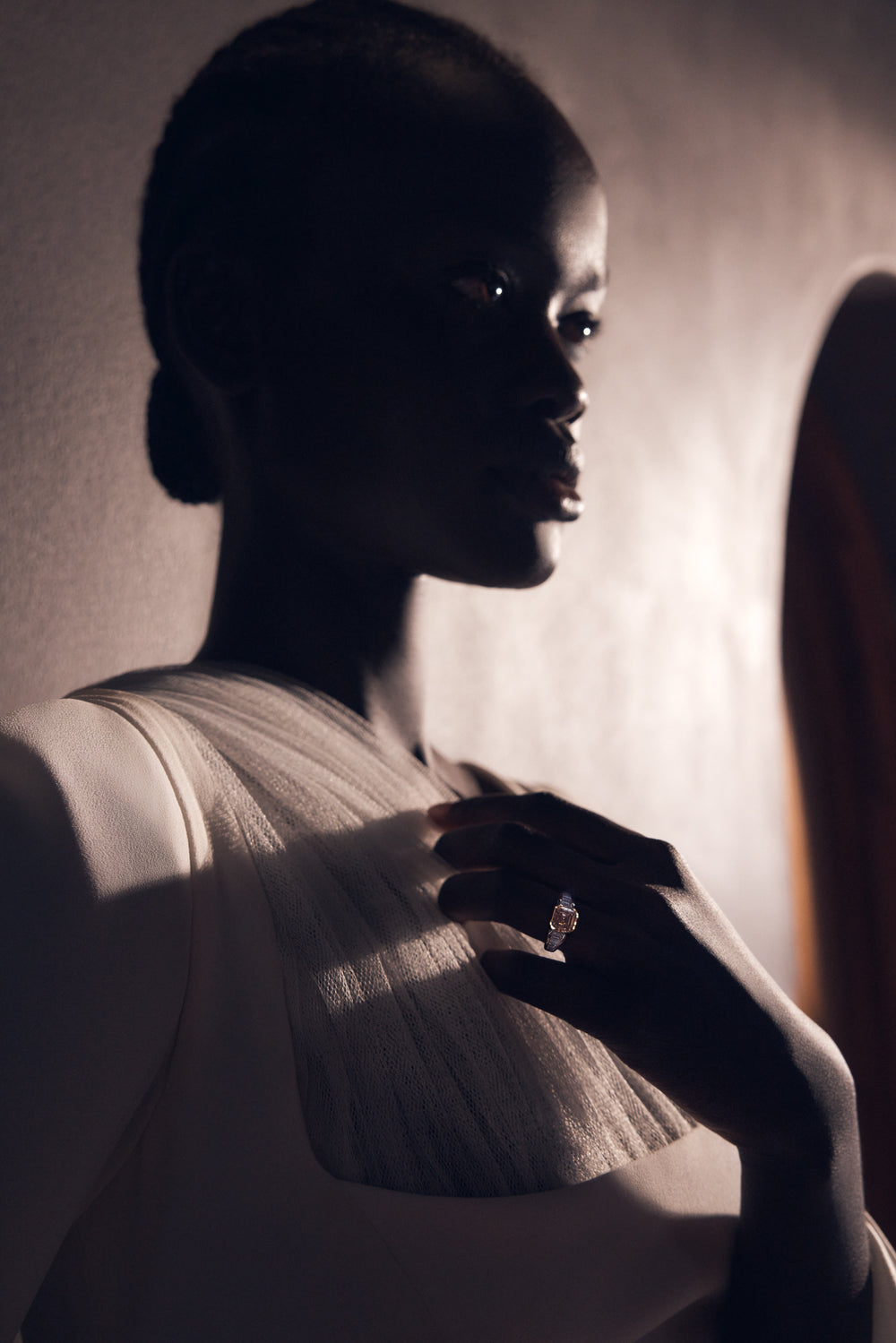 A ring worn on the hand against a sunlit curtain.