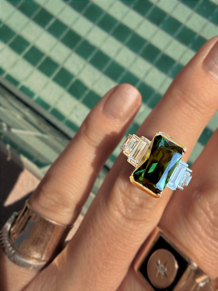 A green sapphire ring with baguette shoulders, worn on the hand