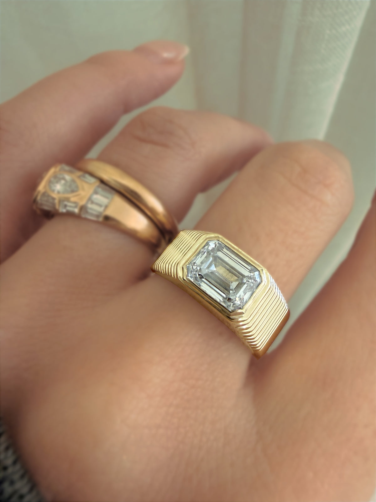An emerald-cut ring and a ridged gold band worn on the hand.